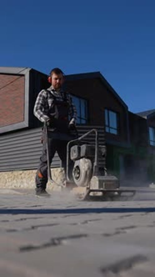 Worker Operating Plate Compactor on Paved Street