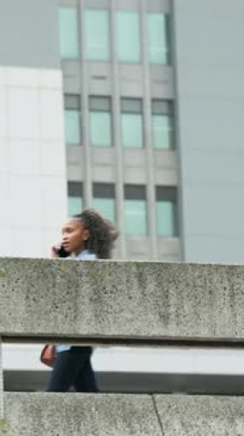 Vertical video: Walking woman in blue top on phone on office walkway, man entering with bag