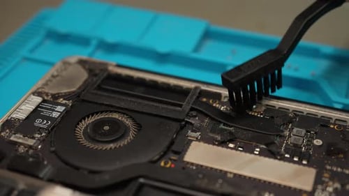 Techniker reinigt die Hauptplatine eines zerlegten Laptops mit einer Bürste und führt wichtige Wartungsarbeiten durch