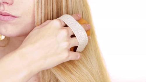 Close up of the straight blond hair of a young woman while brushing their natural brush.
