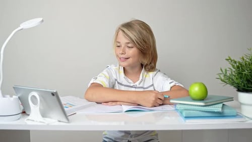 Middle School Smiling Student Boy Sitting at Desk Remote Studying Writing Book Homework and Tablet