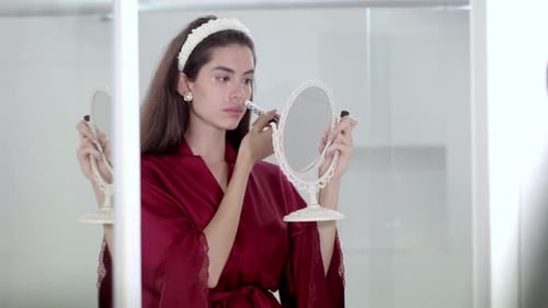 Woman Applies Makeup in Bathroom With Handheld Mirror