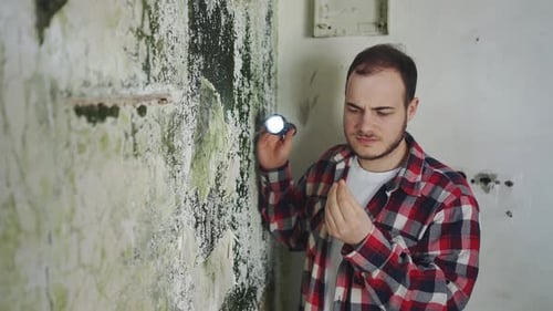 Man Inspects Moldy Wall with Flashlight Indoors