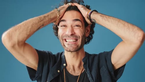 Close up, wonder man put his hands on head looking at camera isolated on blue background