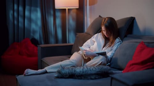 Woman Reads on Couch with Cat at Home