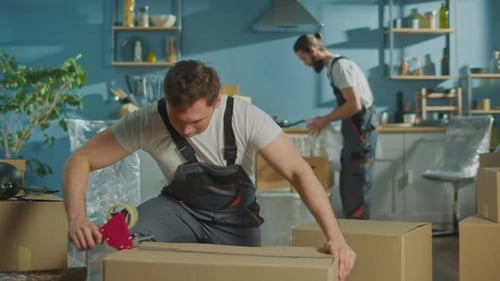 Worker of Moving Company Using Duct Tape Machine for Packing a Cardboard Box