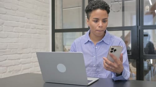 Adult Works At Laptop Holding Cellphone In Office