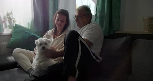 Couple Petting Small White Dog on Living Room Sofa