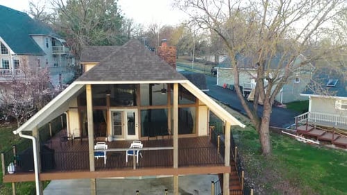 Aerial Drone of Midcentury Modern Cabin Style Home with Large Windows, Deck and Patio. Grass Backyar