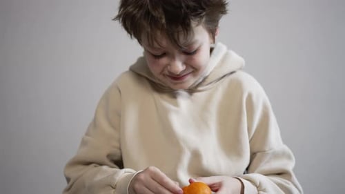 Smiling Caucasian kid peeling the tangerine. Healthy lifestyle, child consuming fruit at home.