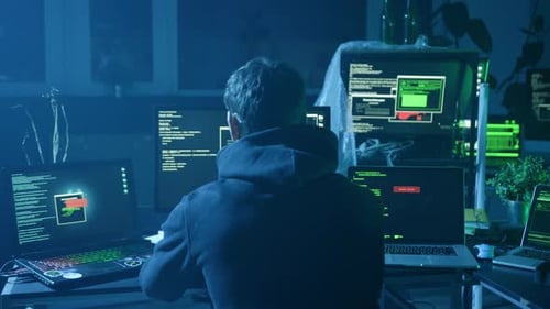 A Mysterious Hacker Enveloped in Shadows Surrounded By Multiple Computer Screens Looms Large