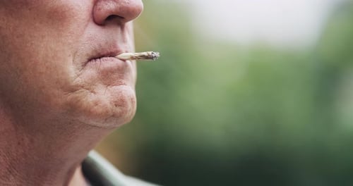An unrecognizable senior man smoking marijuana in his garden at home