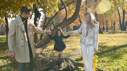 Happy family in an autumn park. Mother and father playing and walking with daughter, yellowed trees