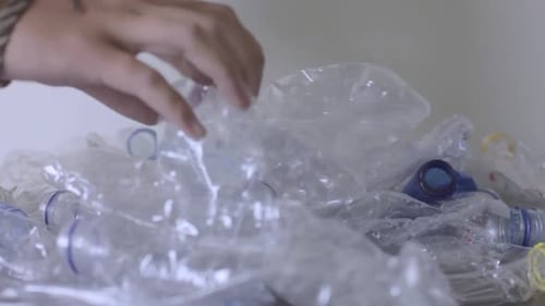 Hands Add Empty Plastic Bottles to Pile