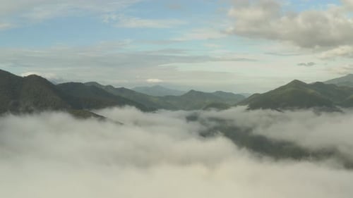 Flying through the clouds above green mountain tops. Aerial view of foggy rainforest