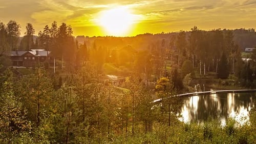 Golden sunset behind forest trees in idyllic scenery with lake and holiday apartments - time lapse