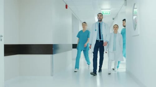 Team of Doctors, Surgeons and Nurses Walk Through Busy Hospital Hallway, They Talk about Patients,