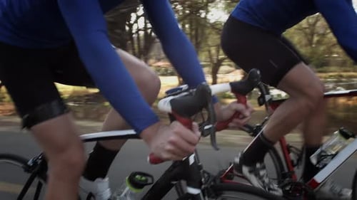 Two young male athletes cycling fast on a road bike at sunset in golden sunlight