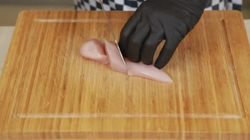 Trancher un filet de poulet cru sur une planche à découper en bois