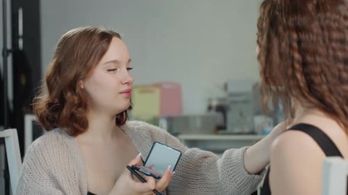 Two women in kitchen, one doing the other's hair
