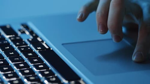 Hands Use Illuminated Laptop Trackpad at Night