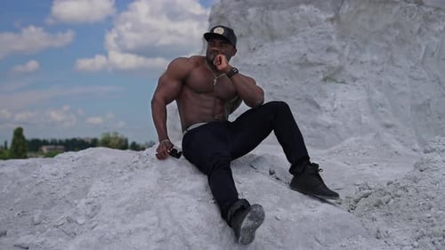 Un hombre pensativo de piel negra sentado sobre una piedra blanca.