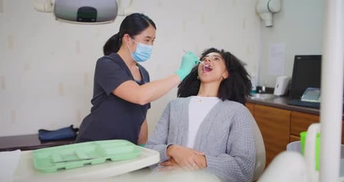 Zahnarzt mit Gesichtsmaske überprüft die Zähne einer Patientin mit einem Spiegelwerkzeug während eines Zahnarzttermins