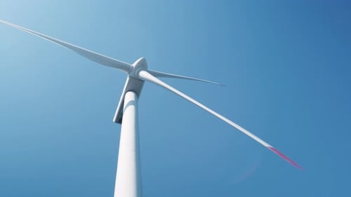 Large wind turbine in field against blue sky on sunny summer day slow motion