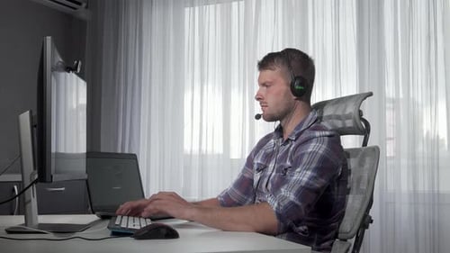 Man Working at Computer Wearing Headset at Desk