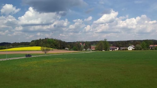 A car drives through the rural landscape of Upper Palatinate, passing green fields and yellow rapese