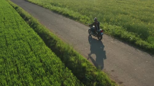 Motorbiker Rides on Asphalt Road Past Hangar and Field