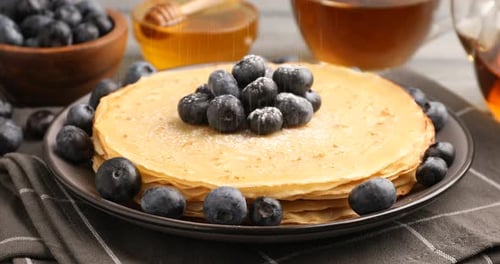 Sieving sugar powder onto delicious crepes at table, closeup