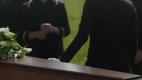 Mourners Gathered Around Coffin Outdoors in Grassy Field