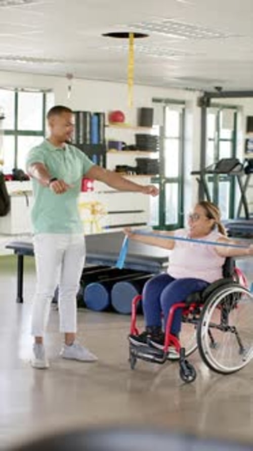 Vertical video: In rehabilitation center, exercising with resistance band, woman in wheelchair and t