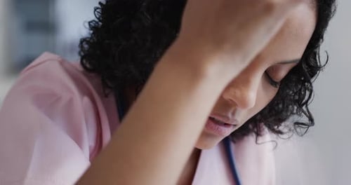 Stressed biracial female nurse leaning on wall in hospital in slow motion
