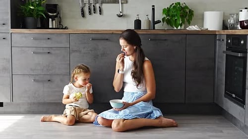 Mother and Daughter Eating Apples on Kitchen Floor