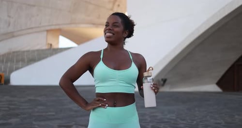 Athletic woman holding reusable water bottle outdoors smiling