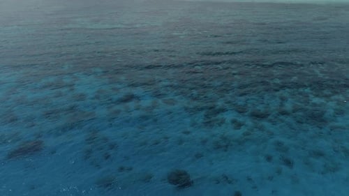 Small Fishing Boat Floating on Calm Blue Ocean Above Reef Patterns, Aerial