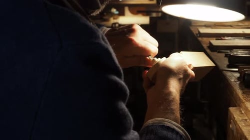 Luthier shaping and fitting wooden pegs on a new violin scroll under warm workshop light