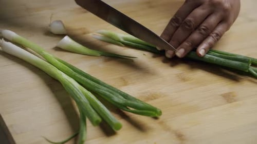 Trimming Fresh Green Onions on a Wooden Board for Cooking Preparation