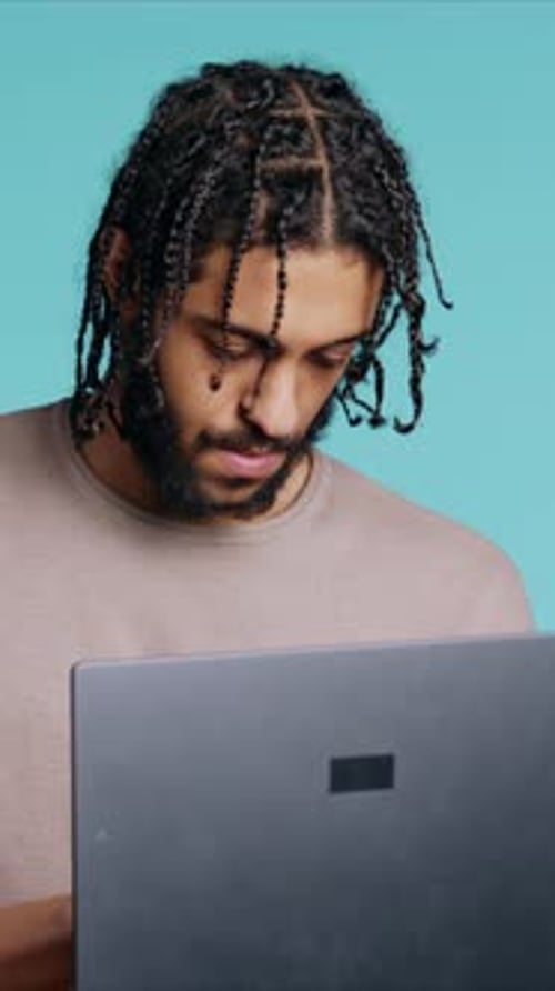 Vertical Video Man Inputting Data on Laptop While Standing in Blue Studio Background