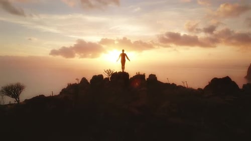 Person standing on a rocky cliff at sunset and exercising with the ocean in the background
