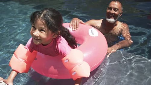 Uma garota birracial com bóias de braço aproveita o tempo na piscina com o avô
