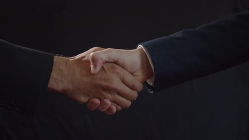 A Strong Male Handshake Hands in Business Suits on a Black Background