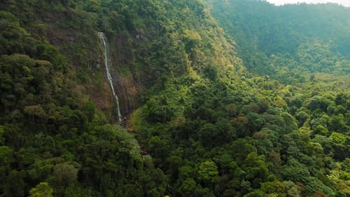 Waterfall Cascading Through Dense Rainforest Surrounded By Steep Green Hills