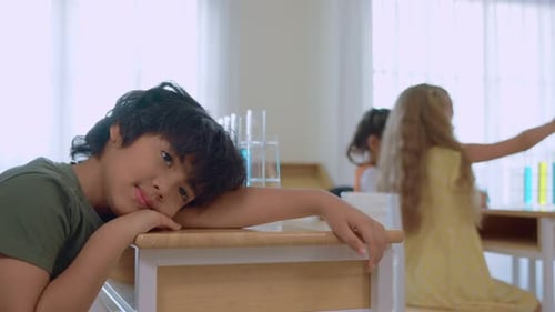 Adorable young boy student sleeping on study table at elementary school.