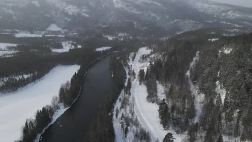 Flying over valley in Southern Norway in snow. Mountains covered in snow, river and road along the