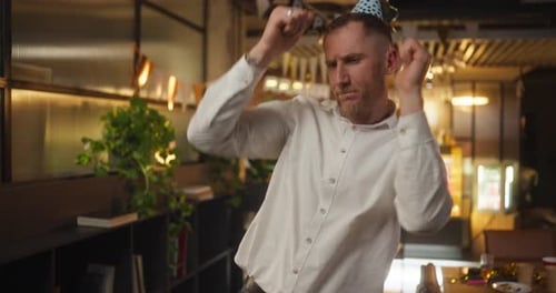 Um cara loiro feliz em uma camisa branca dança e se diverte durante um feriado corporativo no escritório