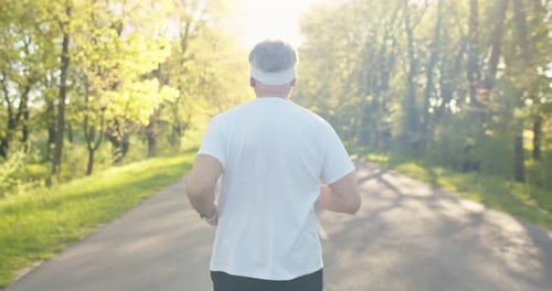 Rear of Caucasian Senior Sportsman Jogging Outdoors Alone on Street Greyhaired Old Male Athlete