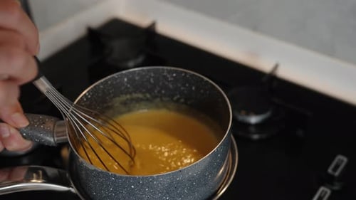 The cook stirs the orange puree in the saucepan as it heats up on the steam, in a close-up, slow mo